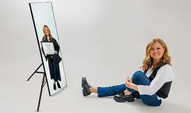 A photo with a white background showing Mackenzie sitting on the ground and in a mirror dressed in a graduation cap